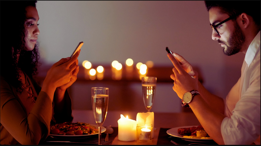 Photo of two people looking at their phones on a dinner date.