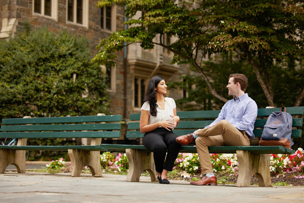 2 students talking on a bench outside Healy Hall