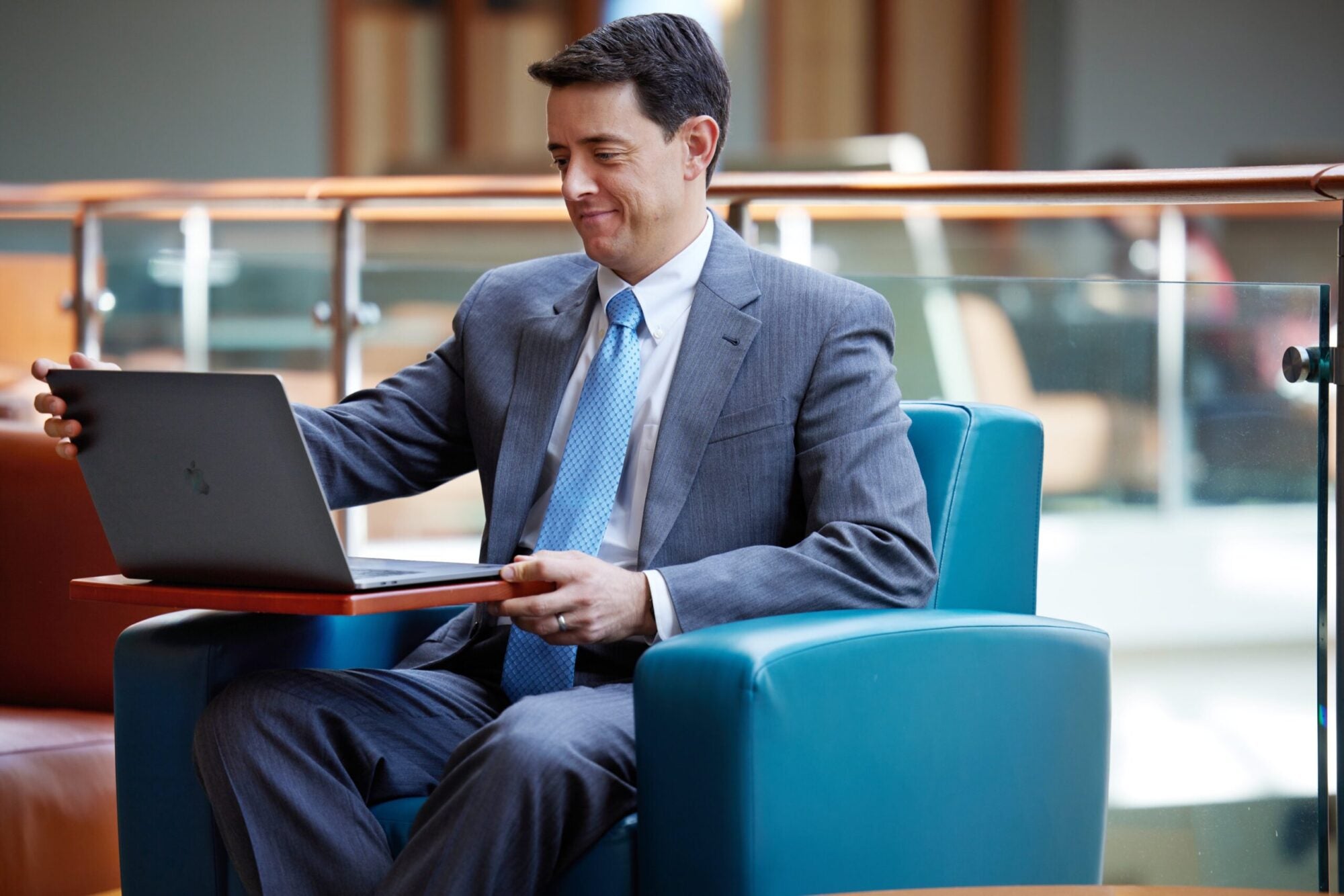 EMBA student sitting in blue chair looking at laptop