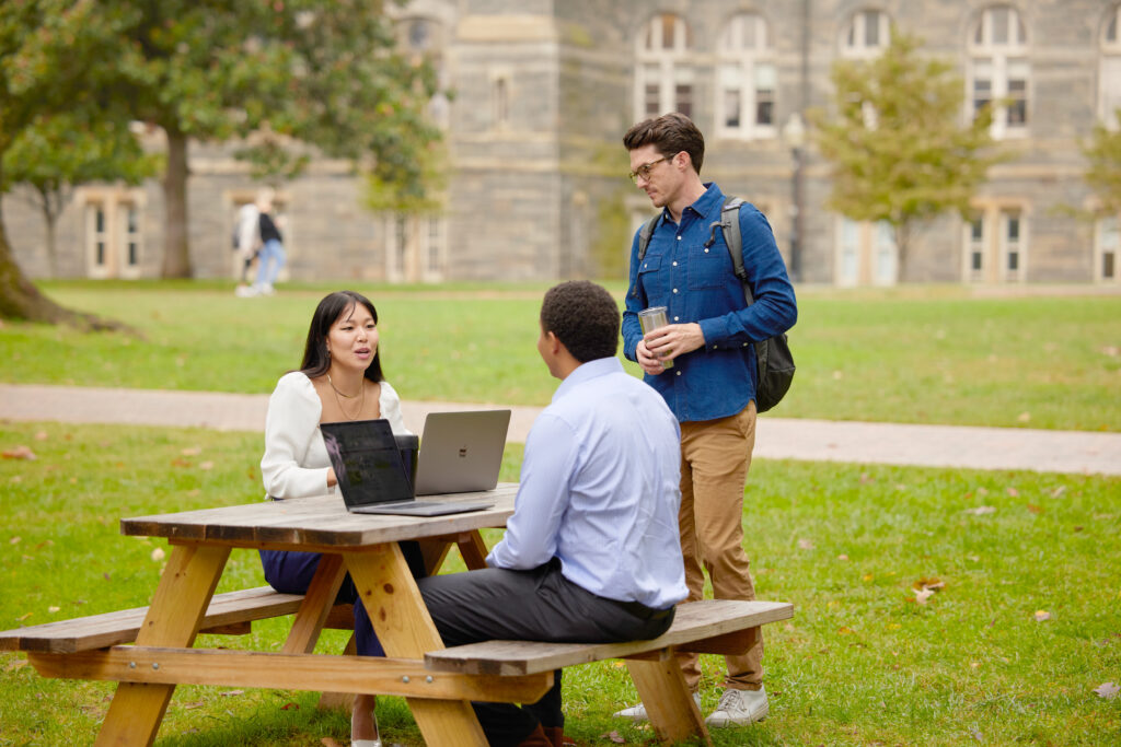 3 MBA students sitting on laptops on Healy Lawn