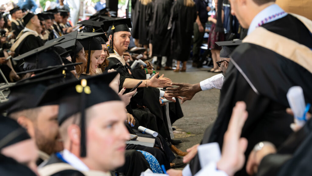 McDonough School of Business graduates during commencement high fiving their peers as they walk past their row of seated classmates