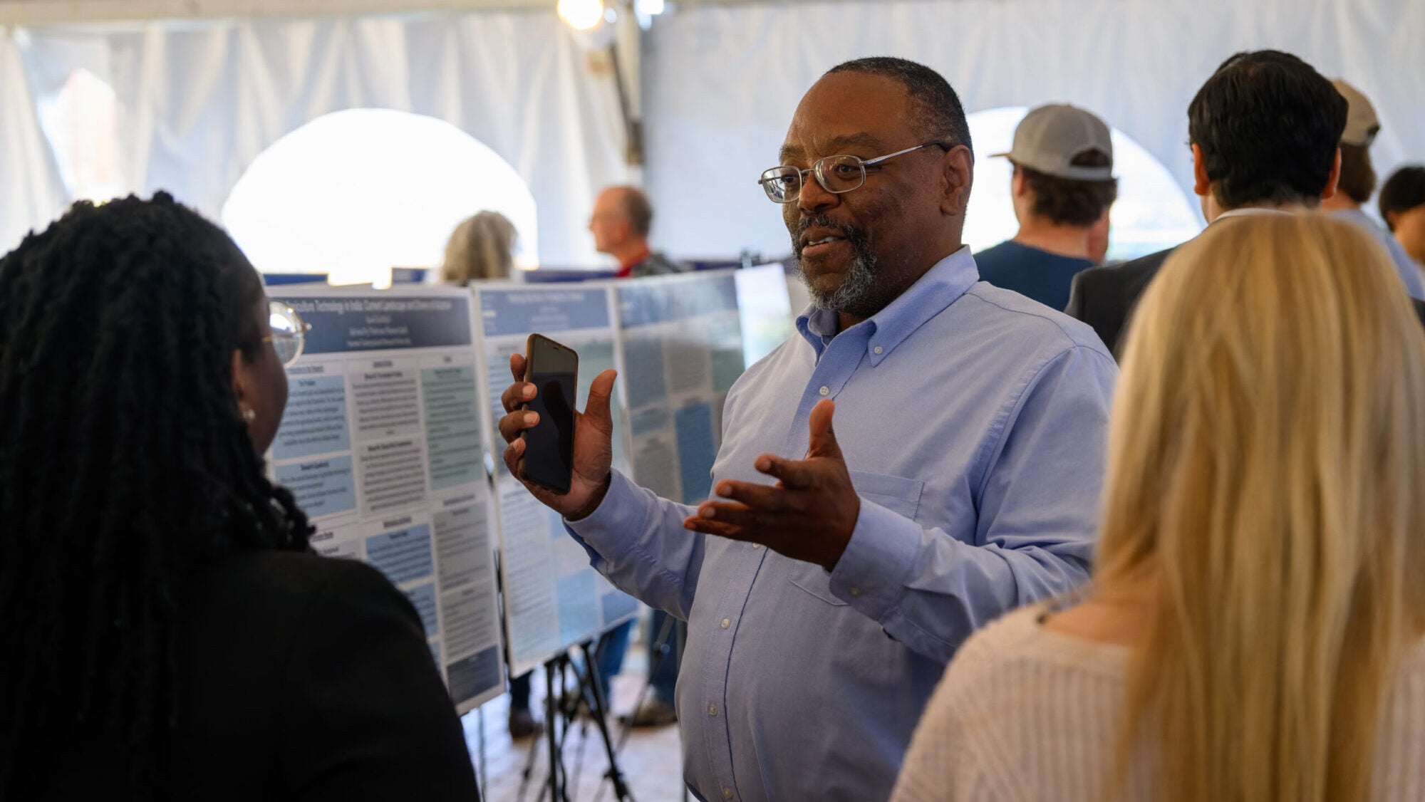 Professor George Comer speaking to undergraduate students outside under a white tent