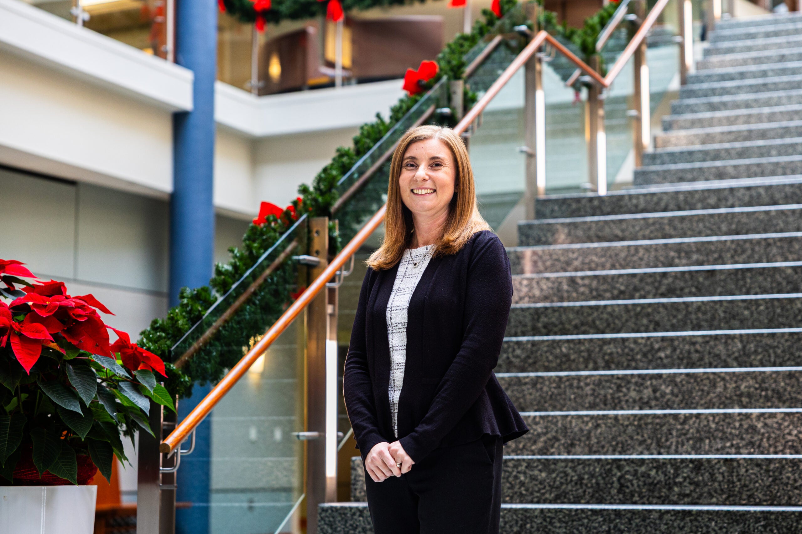 Teresa Mannix stands at base of Hariri Building stairs and the railing is covered in garland