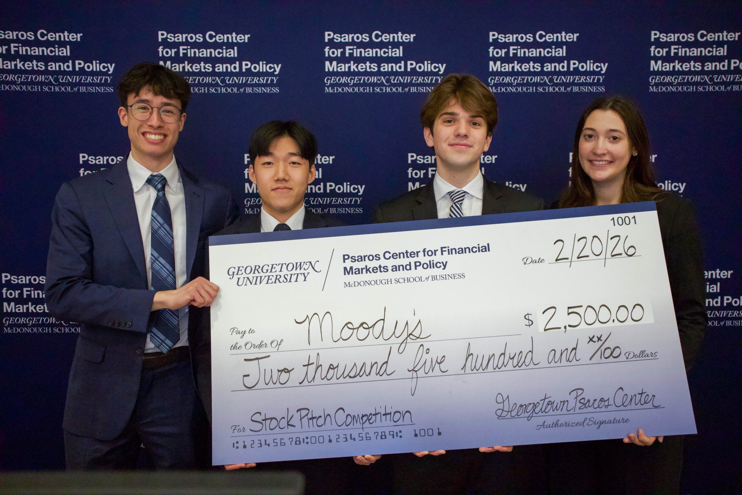 Four undergraduate Georgetown McDonough students stand in front of a Psaros Center banner holding a check won at a pitch competition