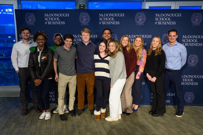 Georgetown students gather for a group photo in front of McDonough School of Business banner