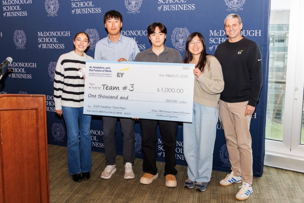 Georgetown students, two EY representatives, holding a large cardboard check