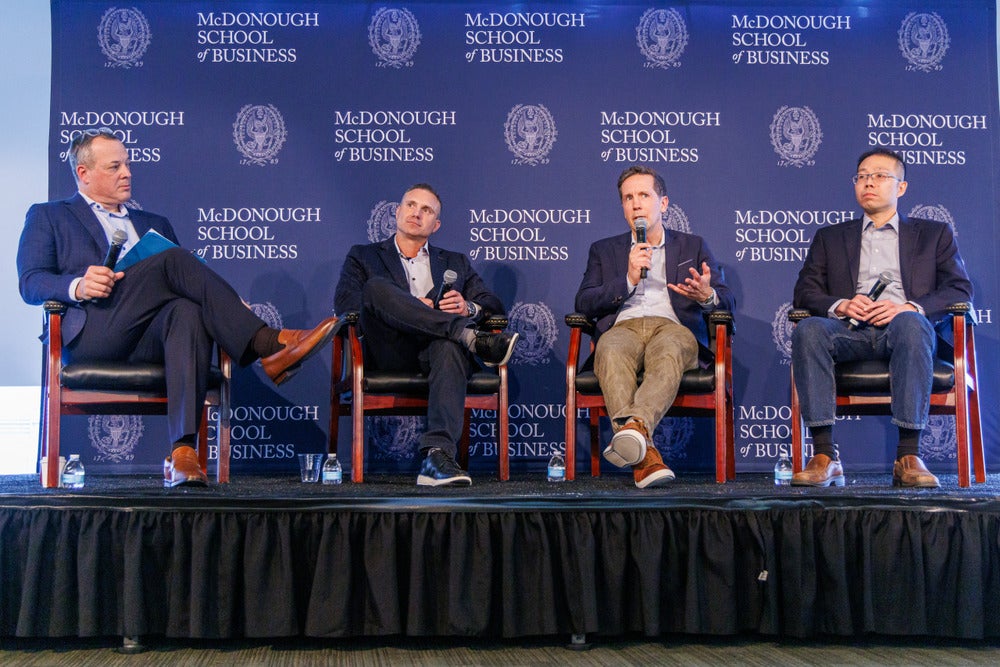 Panel of men on stage in front of Georgetown McDonough step-and-repeat for Business of Health Summit