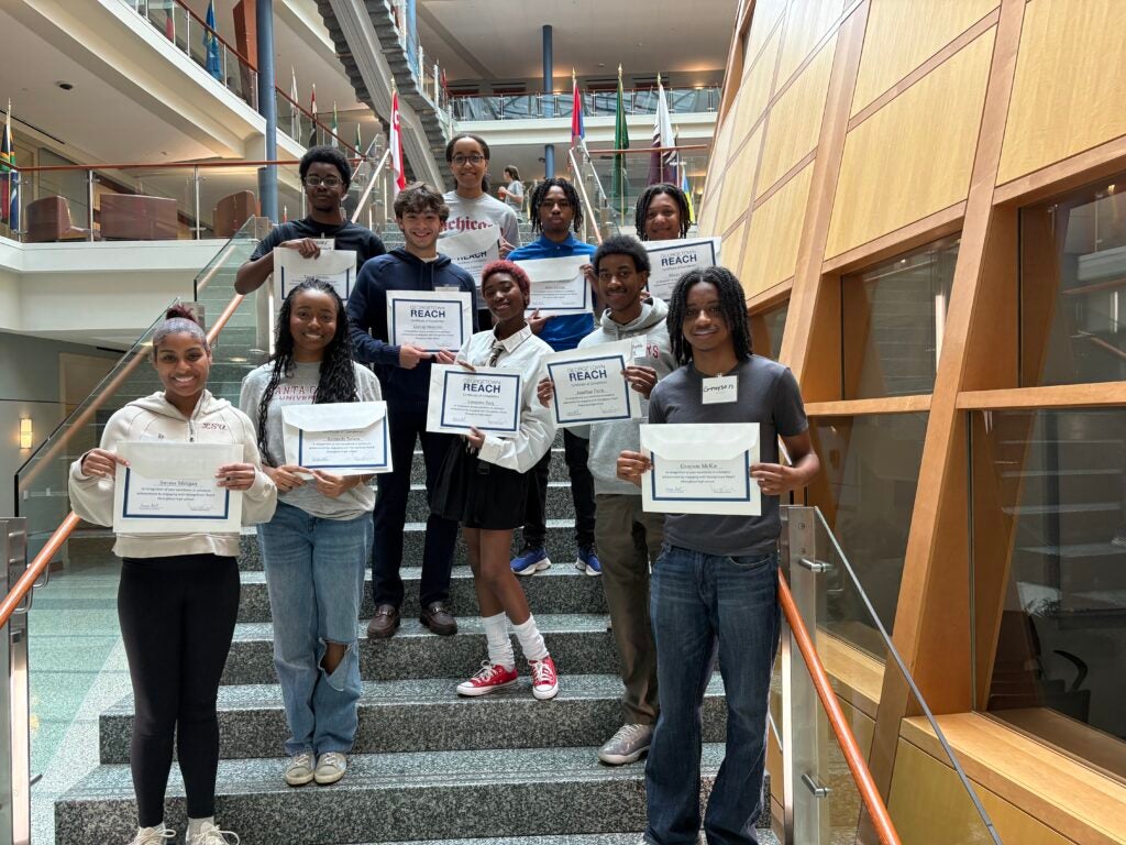 Reach students standing on the stairs of the Hariri building, smiling while holding certificates.