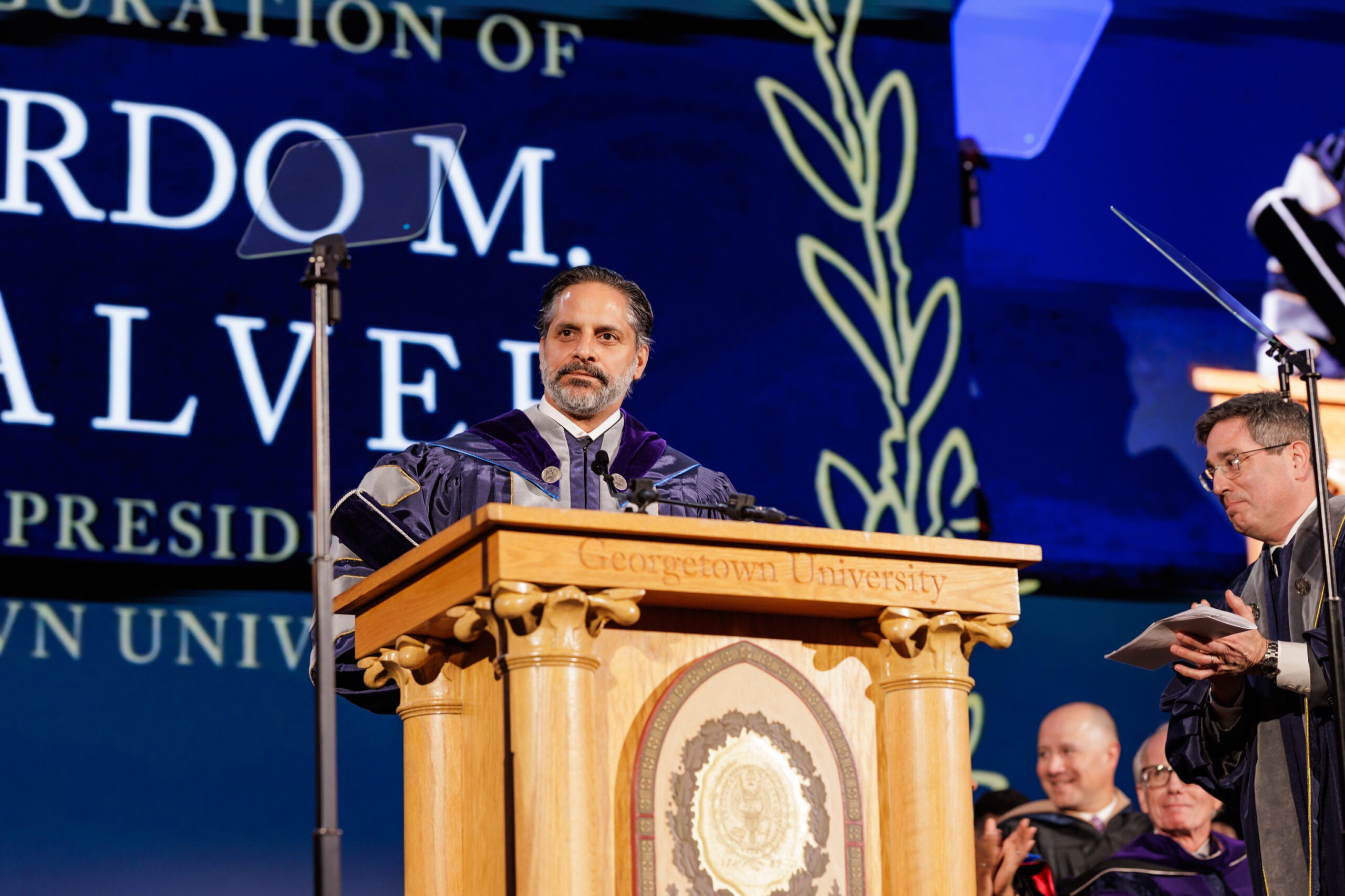Georgetown University president stands behind a podium in blue academic robes